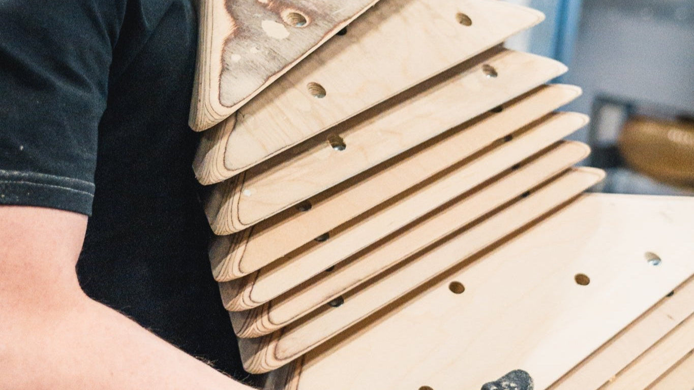 Eine Person die einen Stapel Holzvolumen ohne Beschichtung durch eine Werkstatt trägt.