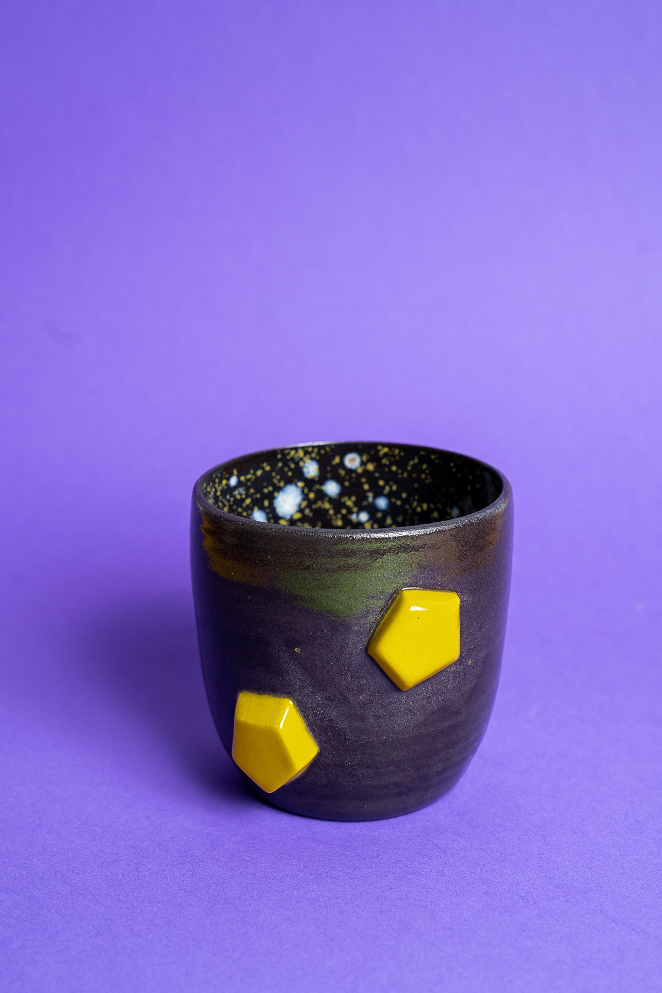 Eine schwarz-violette Tasse mit zwei gelben Banana Volumes Stacks shapes auf der Seite auf violettem Hintergrund.