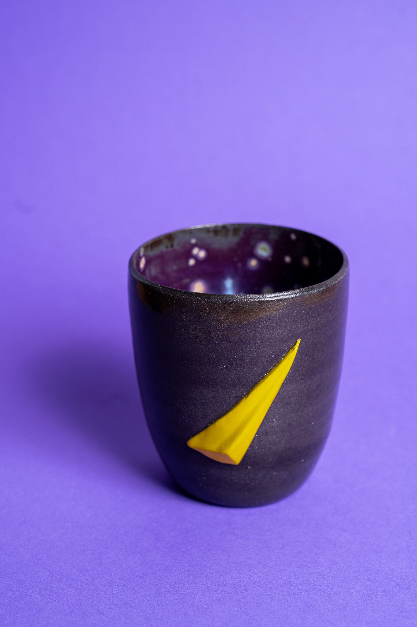 Eine schwarz-violette Tasse mit gelbem Banana Volumes Dreamcatcher shape auf der Seite auf violettem Hintergrund.