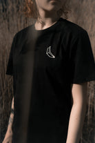 Man sieht den Oberkörper einer Frau, sie trägt ein schwarzes Banana Volumes T-Shirt.